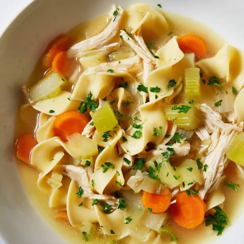 A close-up shot of a comforting bowl of homemade Chicken Noodle Soup garnished with fresh parsley.