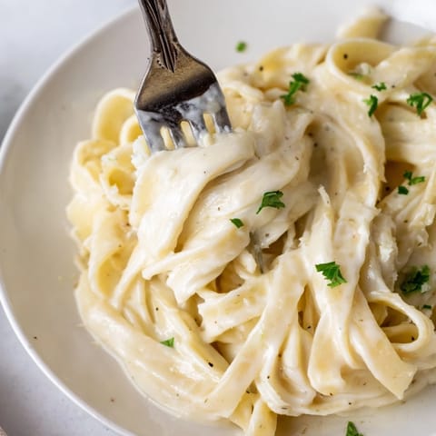 A close-up of Roasted Cauliflower Alfredo pasta in a white bowl, highlighting the velvety texture and melted Parmesan.  