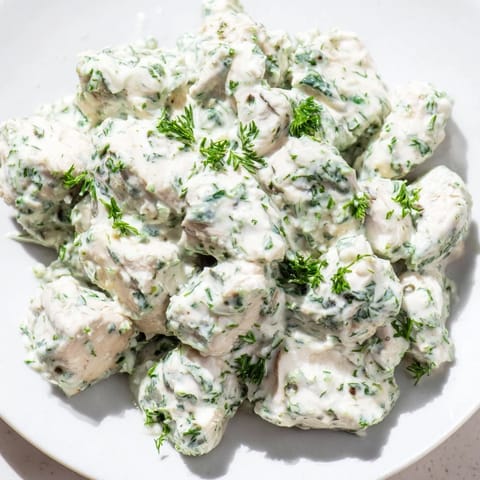 A vibrant bowl of Green Goddess chicken salad with cherry tomatoes, cucumber slices, and a bright herbaceous dressing.