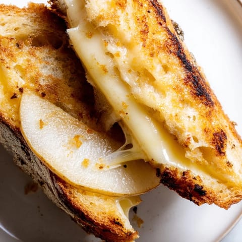 A close-up of a golden-brown smoked Gouda & apple grilled cheese sandwich, showcasing the melted cheese and crisp apple slices between buttery sourdough bread.  