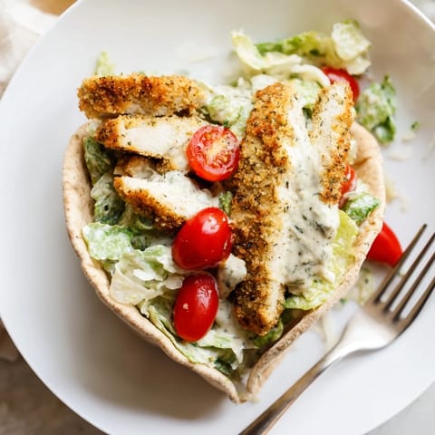A close-up of Crispy Herbed Chicken Caesar Pitas with a crunchy panko crust and creamy dressing drizzled on top.  