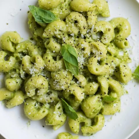 A fork twirls tender macaroni coated in vibrant green avocado pesto sauce, ready to enjoy.  