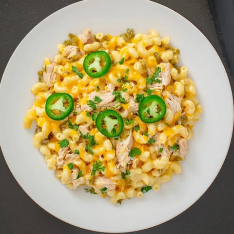 A close-up view of a skillet of creamy Green Chili Chicken Mac, with tender shredded chicken and diced green chiles nestled in cheesy elbow macaroni.
