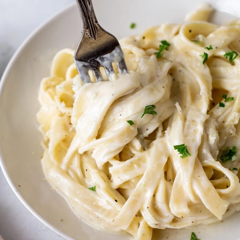 A close-up of Roasted Cauliflower Alfredo pasta in a white bowl, highlighting the velvety texture and melted Parmesan.  