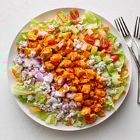 A close-up of a vibrant Buffalo Chicken Chopped Salad, showcasing juicy, sauced chicken pieces atop crisp romaine lettuce with diced celery and carrots.