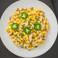A close-up view of a skillet of creamy Green Chili Chicken Mac, with tender shredded chicken and diced green chiles nestled in cheesy elbow macaroni.