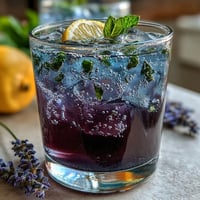 Iced lavender lemonade with fresh mint in a clear pitcher, garnished with lemon slices and mint sprigs, served over ice cubes for a refreshing spring drink.